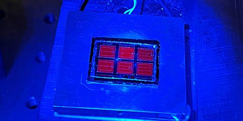 The record-setting solar cell shines red under blue luminescence (photo by Wayne Hicks, NREL).